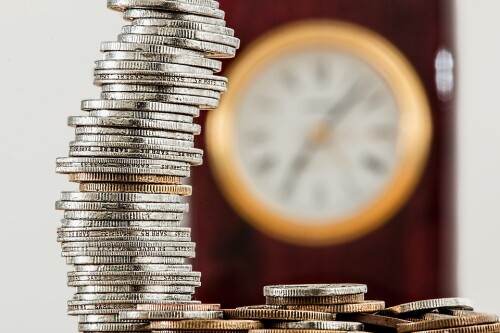 a stack of coins in front of an out-of-focus clock