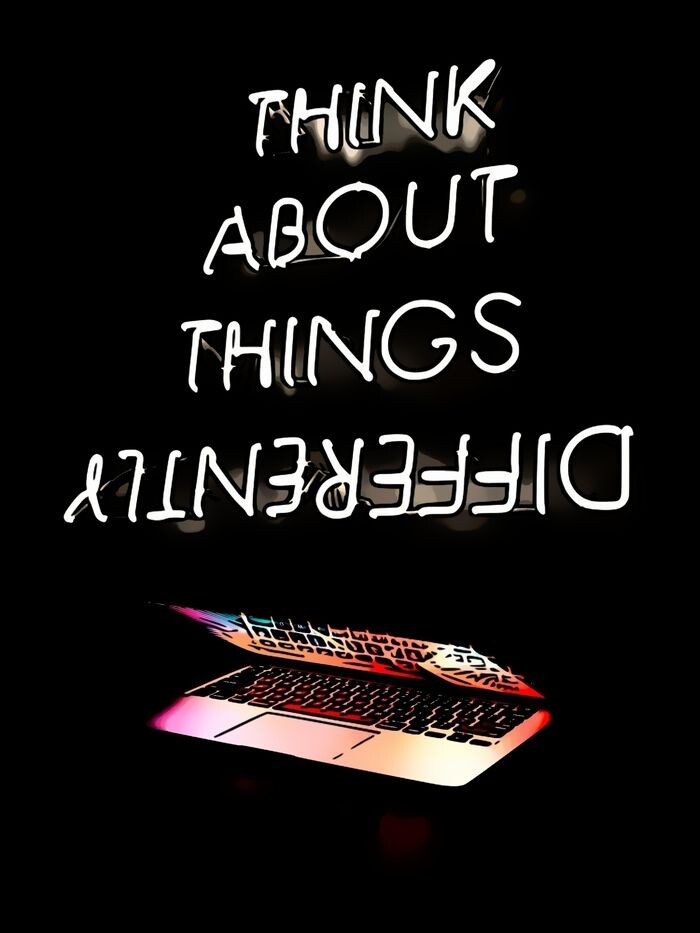 A laptop which is powered up and glowing, below a neon sign which says