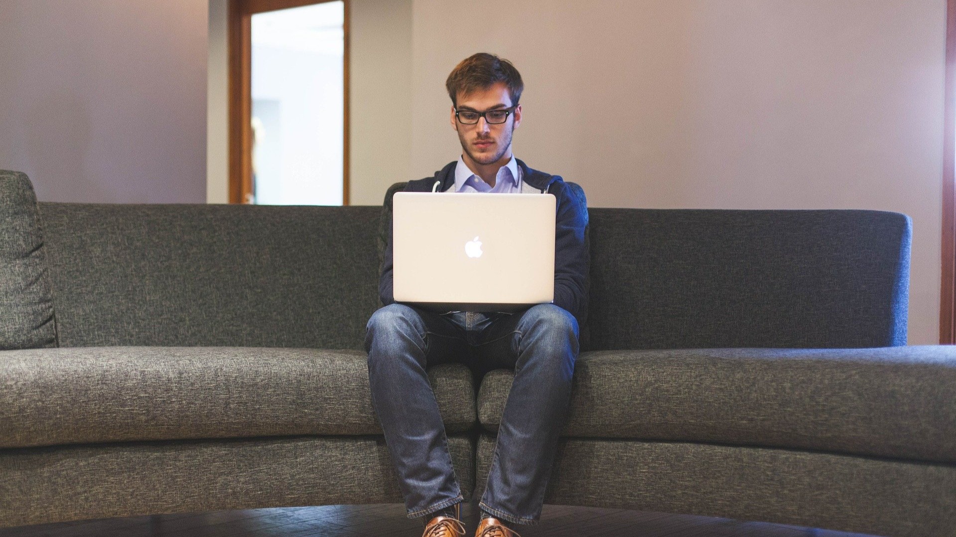 A man sitting in the corner of a couch with his laptop on his lap trading crypto