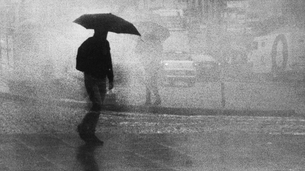 A black and white photo of a man holding an  umbrella in the rain.