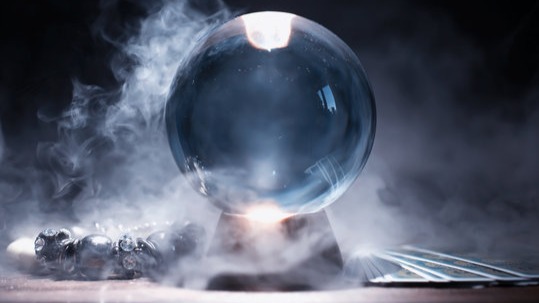 Crystal ball on a stand next to tarot cards and surrounded by smoke