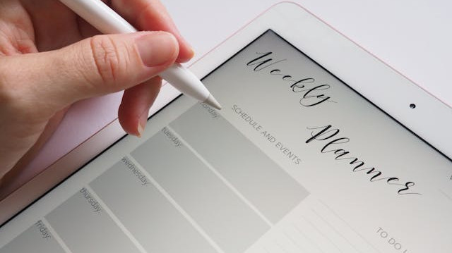 Person holding a white stylus above a tablet showing a weekly planner